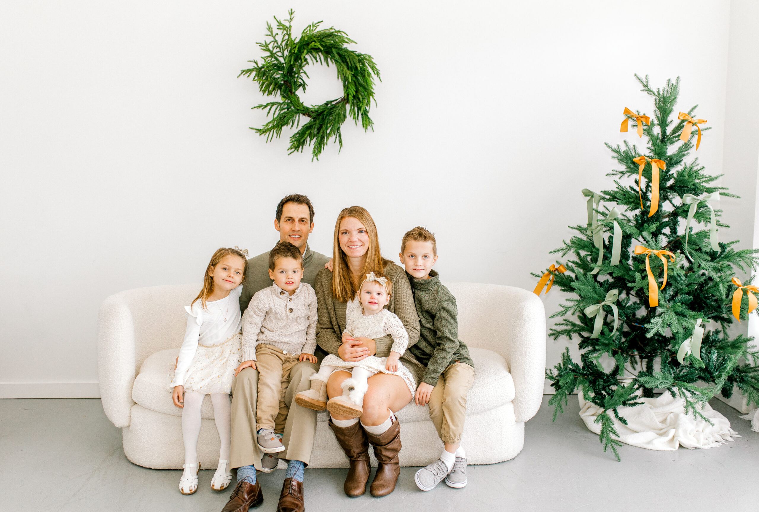 family posing in front of minimalist Christmas backdrop of a white couch and Christmas tree
