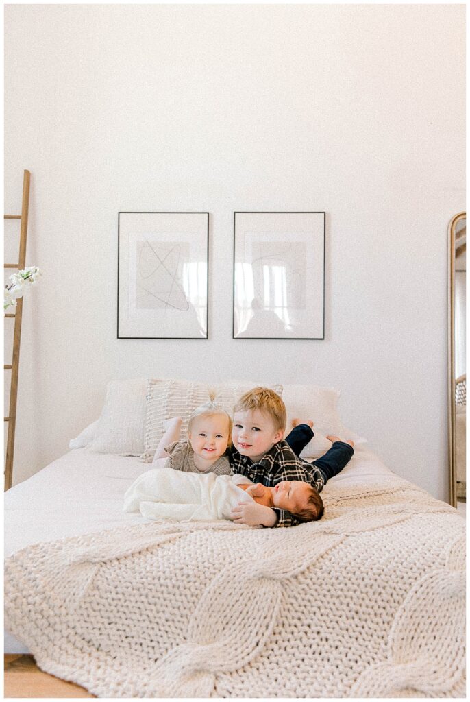 three kids laying on white bed posing for sibling photo