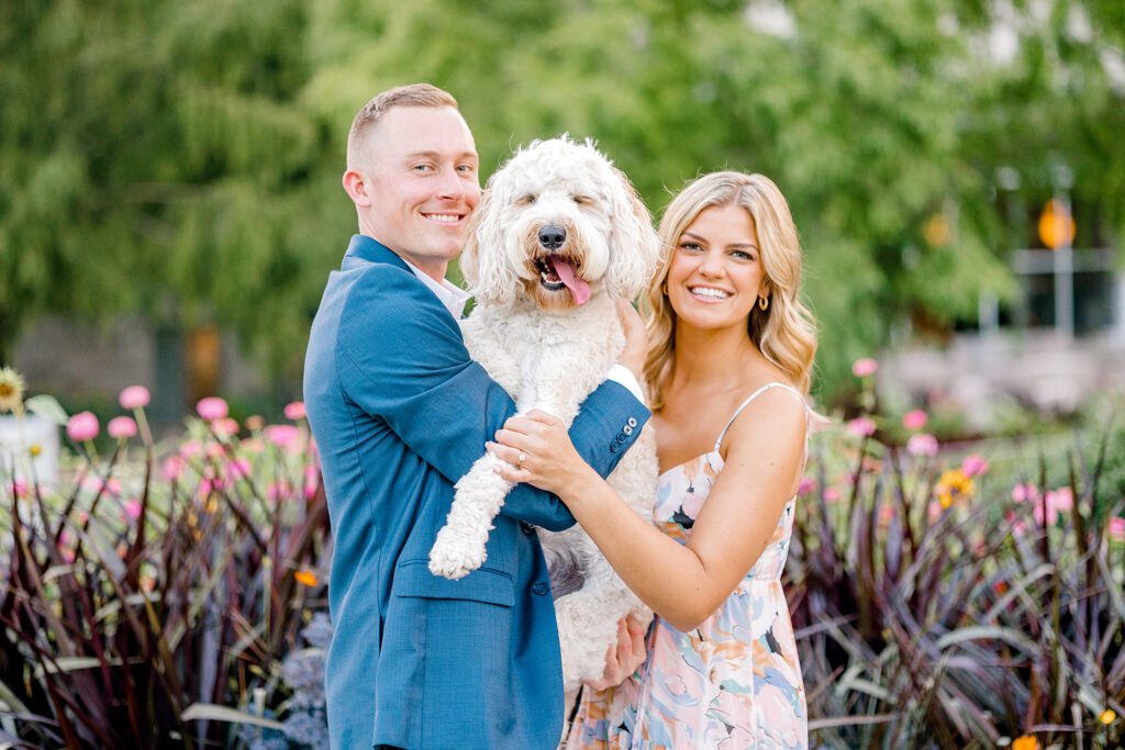 Engaged coupled posing with white golden doodle in front of the fountain at Newfields in Indianapolis