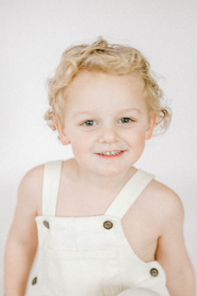 toddler posing in front of white backdrop in photo studio